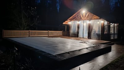 Композитный бассейн с защитным тентом рядом с деревянной террасой и освещённой беседкой ночью